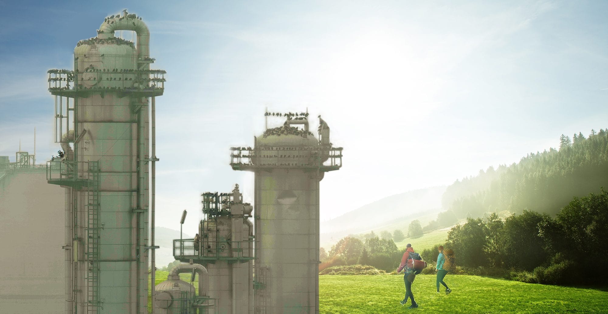 Produktionsanlage, dahinter eine grüne Landschaft, über welche zwei Personen wandern.
