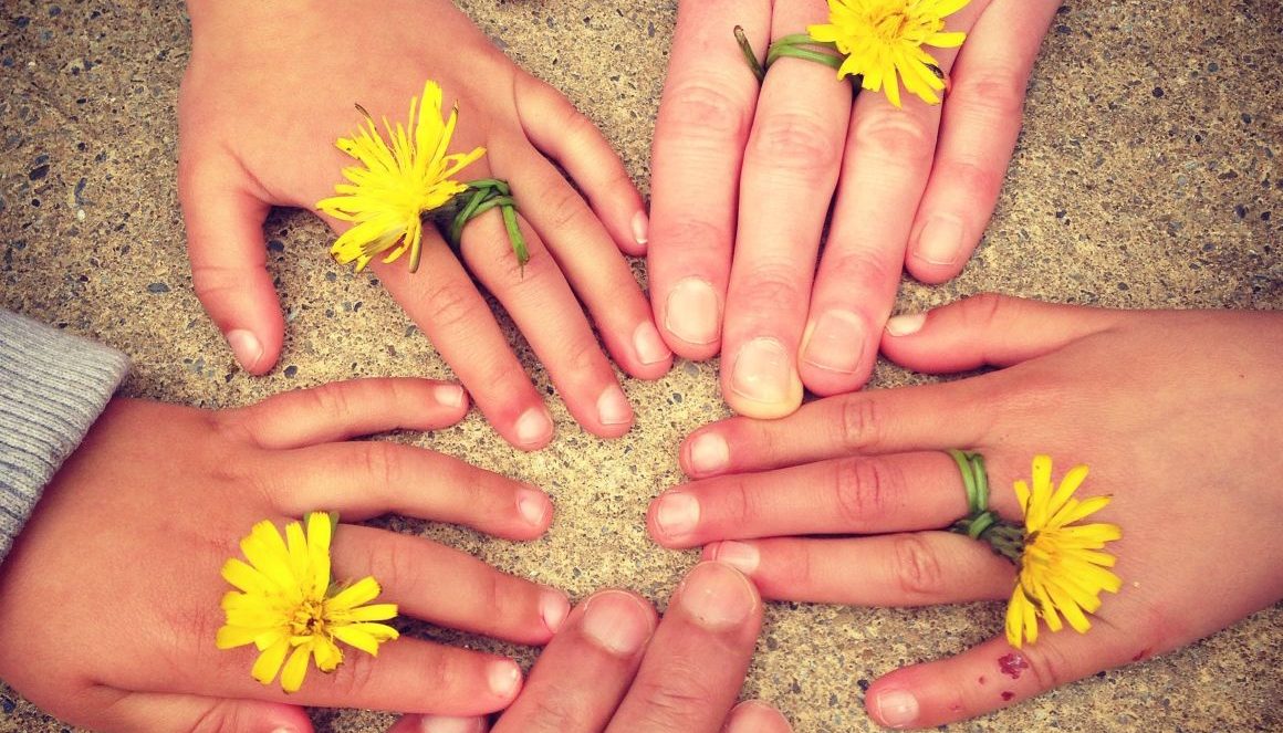 Fünf Hände im Kreis mit Blumen zwischen den Fingern.