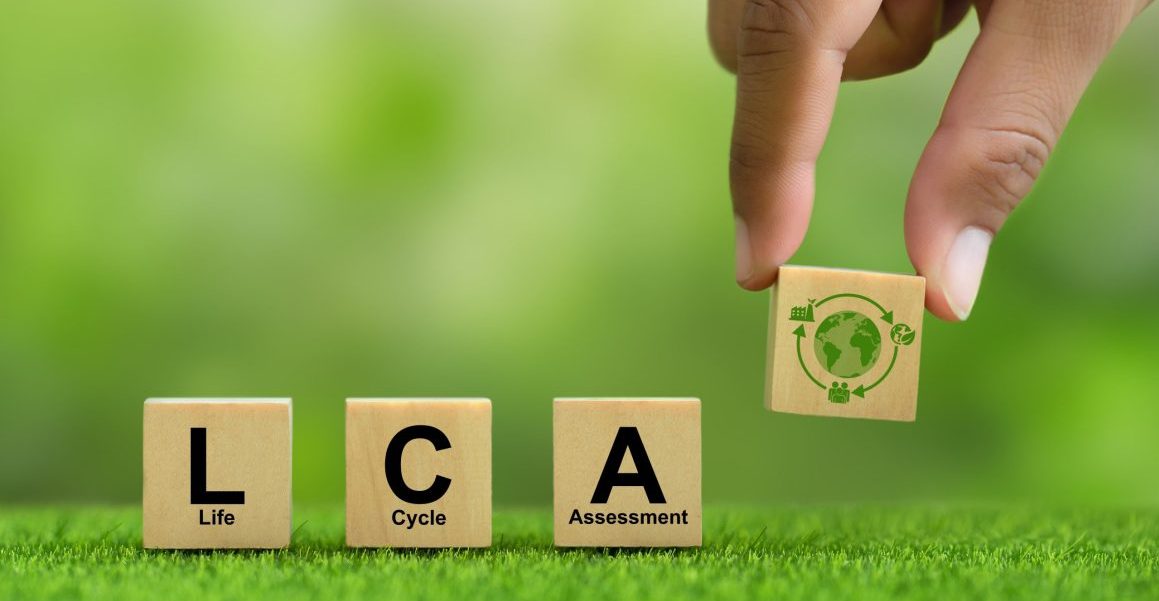 Hand hält hölzernen Würfelblock mit LCA-Symbol auf grünem Hintergrund