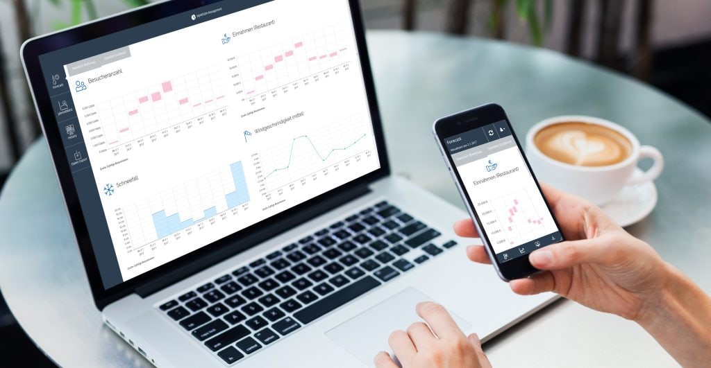 Close-up of a person checking the WEDDA data on their mobile phone, behind them a table with an open laptop and a cup of coffee. Symbolic image for weather risk analysis