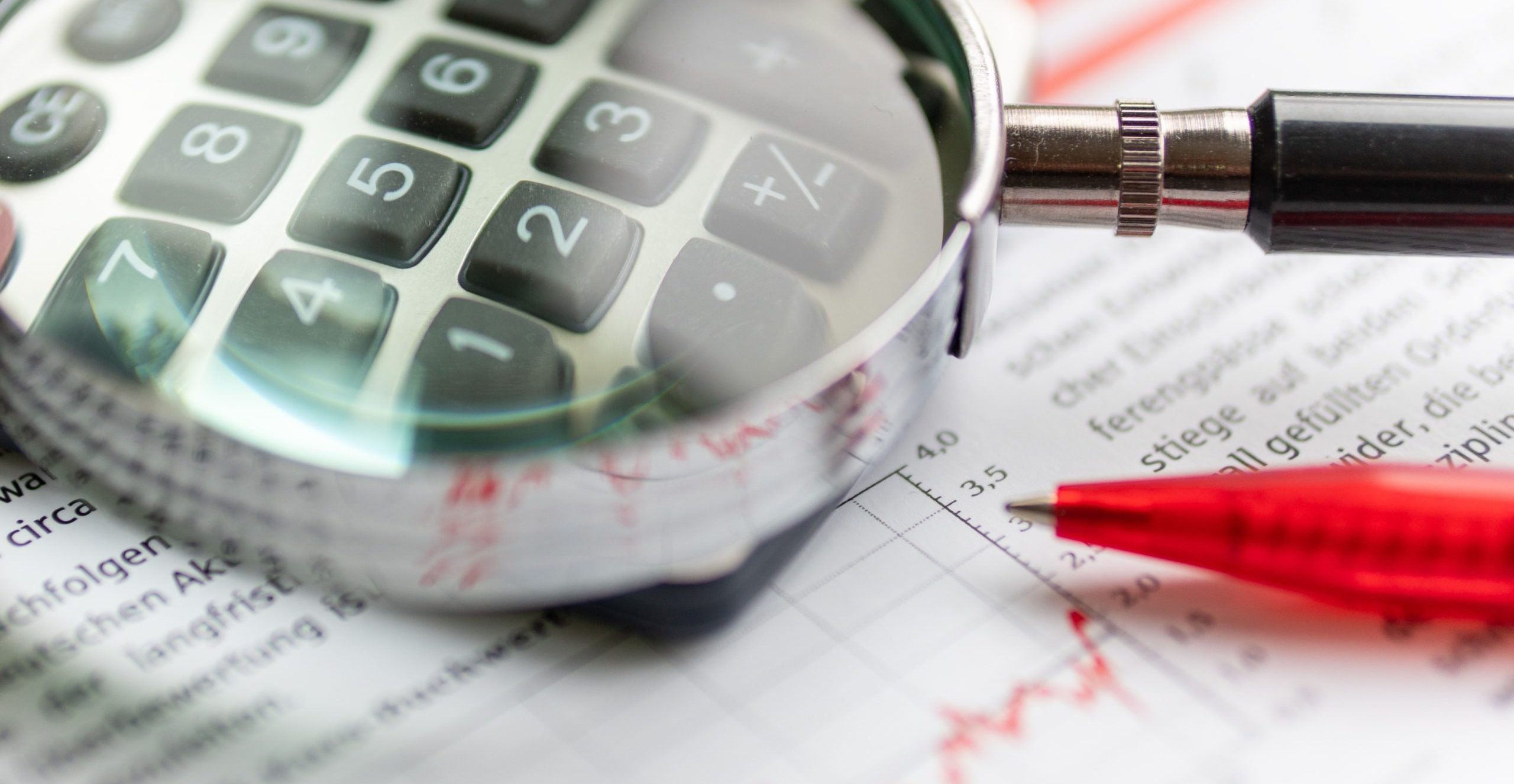 Blick durch eine Lupe auf einen Taschenrechner, darunter ist eine Statistik erkennbar.