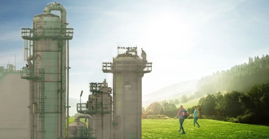 Produktionsanlage, dahinter eine grüne Landschaft, über welche zwei Personen wandern.