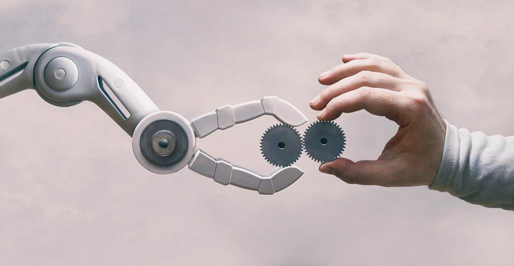 Roboterhand und Menschenhand halten jeweils ein Zahnrad, welche in sich verzahnt sind