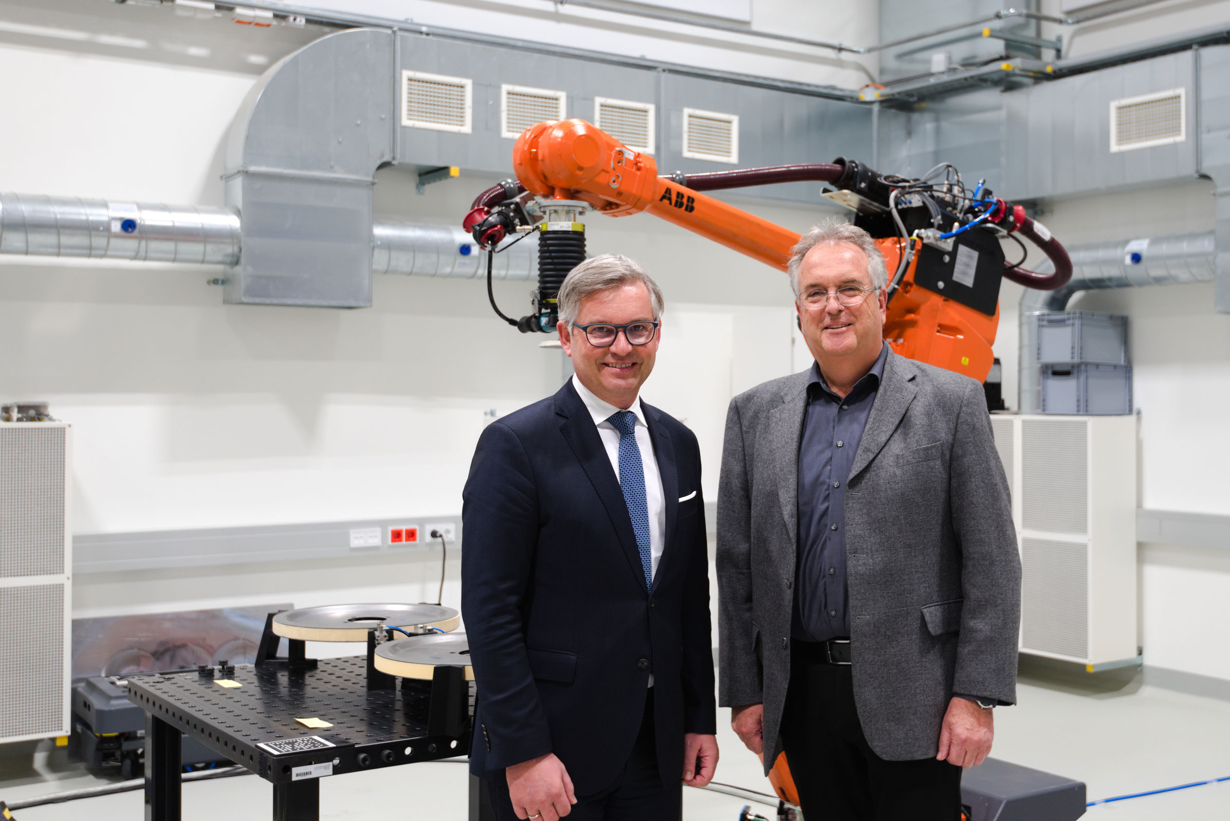 Finanzminister Magnus Brunner steht mit Institutsdirektor Anton Scheibelmasser vor unserem Industrieroboterim ROBOTICS Solution Center.