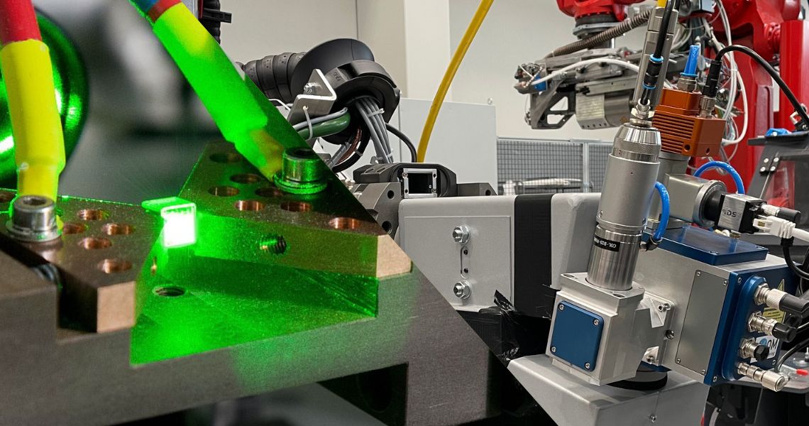 Ein grüner Laser beleuchtet einen präzise eingespannten Kristall in einem optischen Laboraufbau und ein robotergeführter NDT-Testkopf
