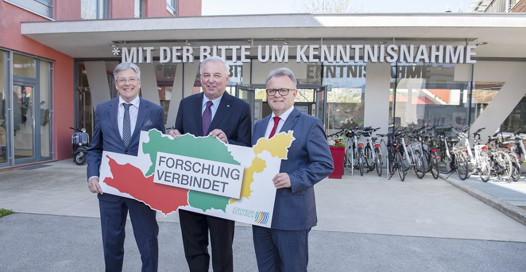 Die drei Landeshauptmänner von Kärnten, der Steiermark und dem Burgenland mit einem Symbol für die Botschaft "Forschung verbindet".
