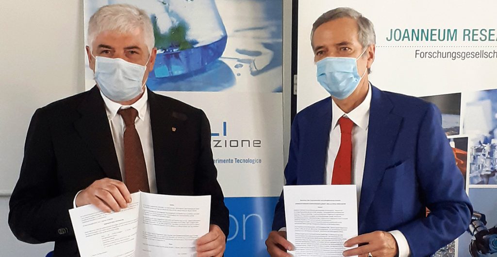 Dino Feragotto, der Vizepräsident der Industriellenvereinigung Udine, und Joanneum Research Geschäftsführer Wolfgang Pribyl stehen vor den Logos ihrer Unternehmen bei der Unterzeichnung des Kooperationsvertrags.