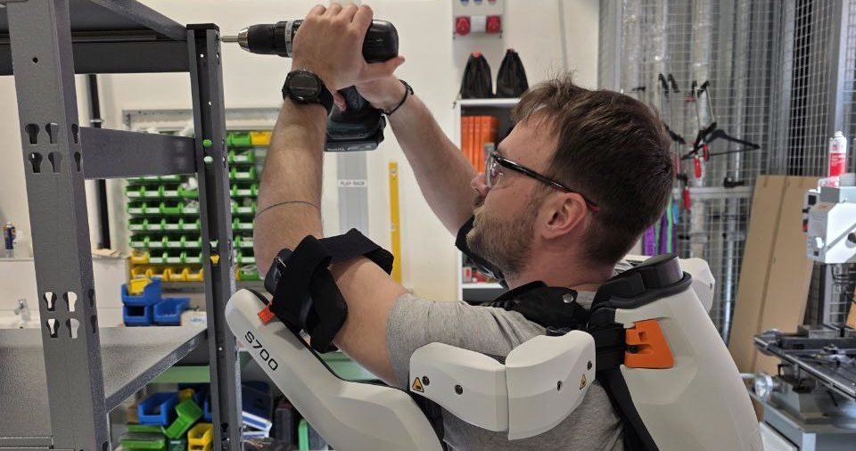 Mitarbeiter steht vor Regal und trägt ein Exoskelett für den Oberkörper